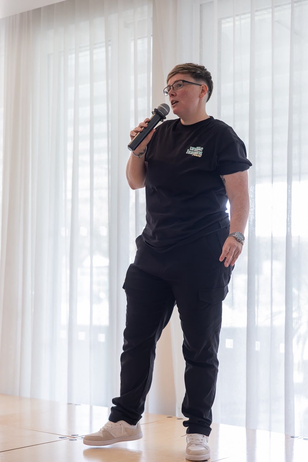 Alex Brown speaking into a microphone on stage at HerHustle Live.