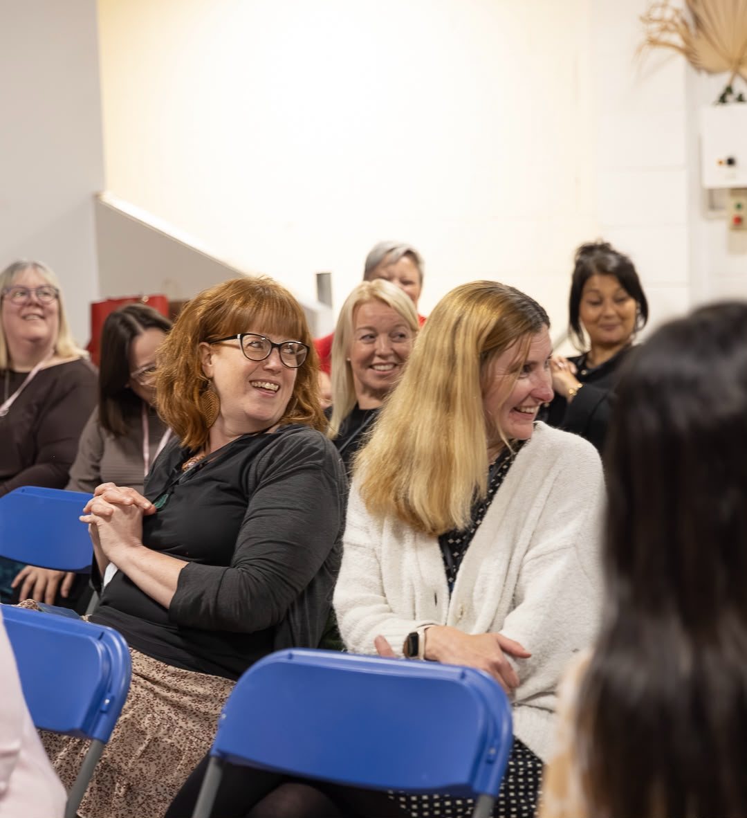 Women in the audience laughing and turning to each other at a HerHustle event.