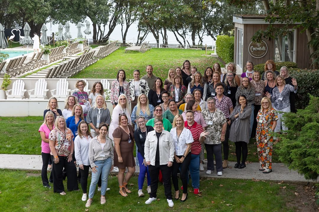 A big group of HerHustle women smiling together for a photo on a hotel lawn.