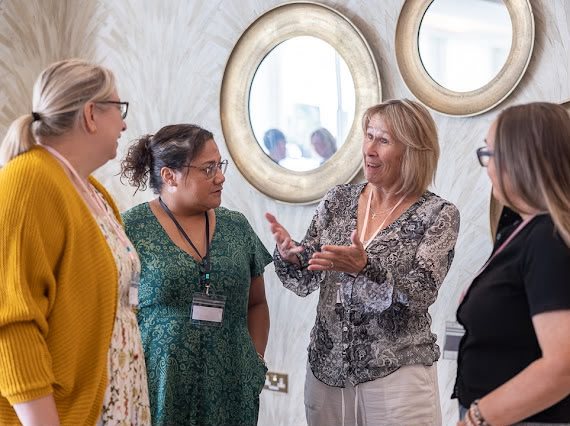 Four women deep in conversation at a HerHustle event, one gesturing as she talks.